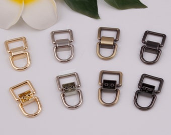 May include: Eight metal D-ring clasps in various finishes, including gold, silver, antique brass, and black. The D-rings are all the same size and shape, with a square frame and a rounded D-shaped loop.