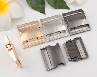 May include: Four metal belt buckles in different finishes: gold, silver, black, and gunmetal. The buckles are all the same size and shape, with a rectangular design and two holes for attaching a strap.