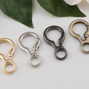 May include: Four metal key rings in different finishes: gold, silver, black, and bronze. Each ring has a swiveling clasp and a small loop.