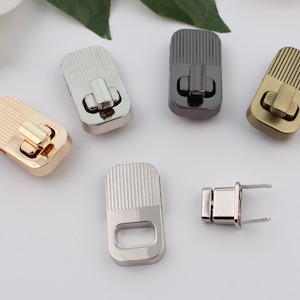 Pode incluir: Cinco fechos de metal em diferentes acabamentos: dourado, prateado, latão antigo, níquel preto e prateado. Os fechos têm forma retangular com um design estriado e um pequeno fecho retangular.