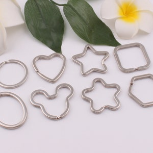 May include: Assortment of silver keychains in various shapes, including a circle, heart, star, Mickey Mouse, flower, square, and hexagon.