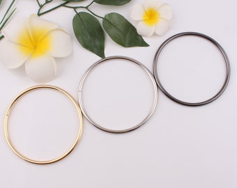 Op de afbeelding: Drie metalen ringen in goud, zilver en zwart. De ringen zijn allemaal even groot en zijn in een rij op een witte achtergrond gerangschikt.
