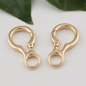 May include: Two gold-toned metal swivel clasps with a small loop on each. The clasps are designed to attach to a bag or other item.