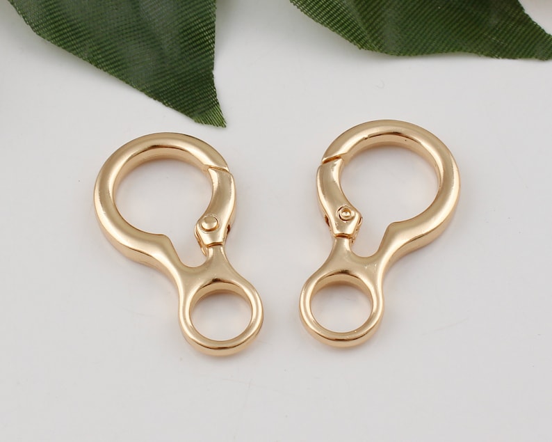 May include: Two gold-toned metal swivel clasps with a small loop on each. The clasps are designed to attach to a bag or other item.