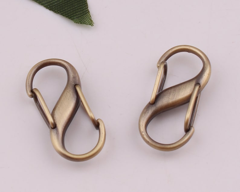 Pu&ograve; includere: Due fermagli o ganci a forma di S in metallo dorato antico. Questi fermagli sono spesso utilizzati per attaccare portachiavi, borse o altri accessori.