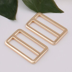 May include: Two gold-toned metal slider buckles. The buckles are rectangular with a single, horizontal bar in the center.