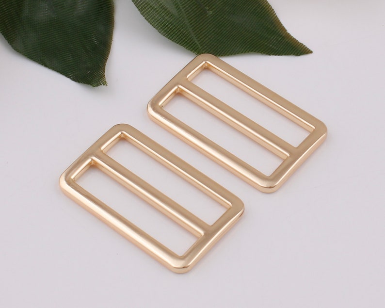 May include: Two gold-toned metal slider buckles. The buckles are rectangular with a single, horizontal bar in the center.