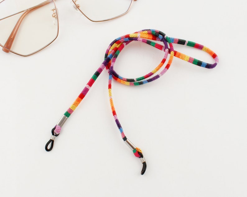Puede incluir: Una cadena de gafas multirrayas colorida con extremos de metal plateado. La cadena est&aacute; hecha de tejido tejido y est&aacute; dise&ntilde;ada para sujetar las gafas de forma segura alrededor del cuello.