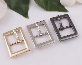 May include: Three metal belt buckles in gold, silver, and black.