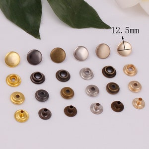 May include: Assortment of 12.5 mm metal snap fasteners in gold, silver, and bronze finishes. The fasteners are in various stages of assembly, including individual caps, posts, and complete snaps.