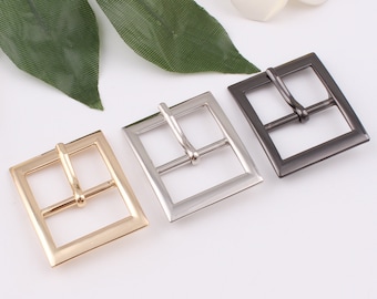 May include: Three metal belt buckles in gold, silver, and black. Each buckle is square shaped with a smooth finish.