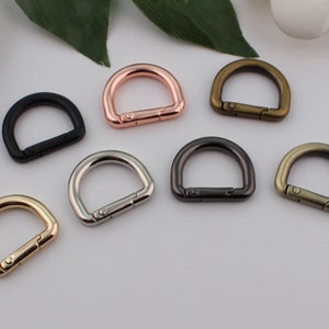 Può includere: Sei anelli a D in metallo di diversi colori. Gli anelli sono tutti della stessa dimensione e forma, ma sono di colori diversi: nero, argento, oro, oro rosa, bronzo e canna di fucile.