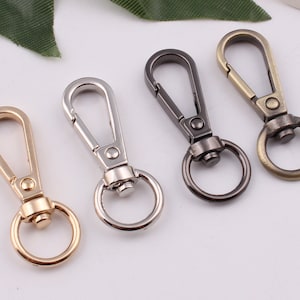 以下が含まれることがあります： 金、銀、黒、ブロンズなど、さまざまな仕上げの金属製のキーホルダーが4つあります。各キーホルダーには、スイベルフックと丸いリングが付いています。