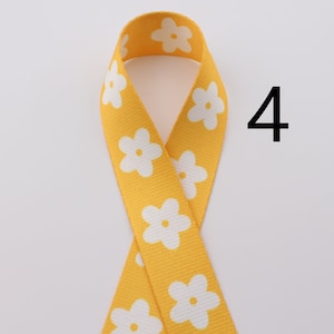 Op de afbeelding: Geel lint met witte bloemenprint. Het lint is gevouwen in een lus en het nummer 4 staat rechts in de afbeelding.