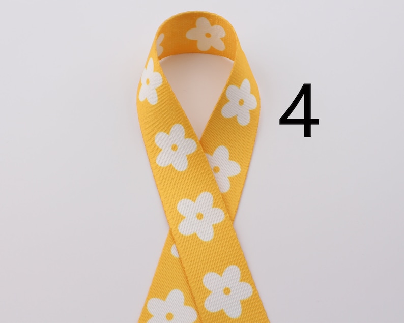 Op de afbeelding: Geel lint met witte bloemenprint. Het lint is gevouwen in een lus en het nummer 4 staat rechts in de afbeelding.