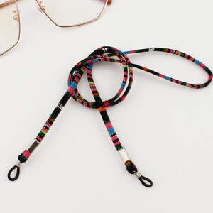 Puede incluir: Una cadena para gafas de color negro y multicolor con extremos de metal plateado. La cadena est&aacute; hecha de cord&oacute;n tejido y est&aacute; dise&ntilde;ada para sujetar las gafas alrededor del cuello.