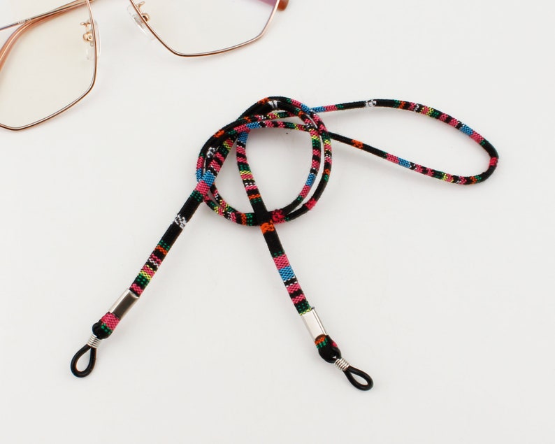 Puede incluir: Una cadena para gafas de color negro y multicolor con extremos de metal plateado. La cadena est&aacute; hecha de cord&oacute;n tejido y est&aacute; dise&ntilde;ada para sujetar las gafas alrededor del cuello.