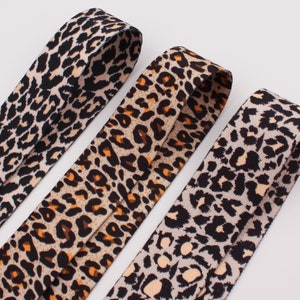 Op de afbeelding: Drie verschillende elastieken met luipaardprint. De elastieken zijn allemaal even breed en hebben een zwarte achtergrond met bruine en beige vlekken.