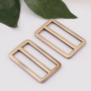 May include: Two gold-toned metal slider buckles. The buckles are rectangular with two parallel slots in the center.