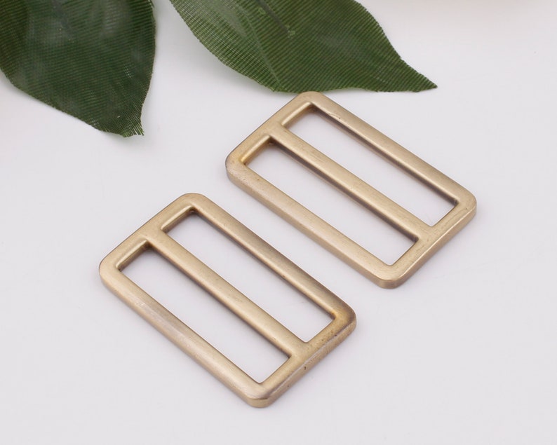 May include: Two gold-toned metal slider buckles. The buckles are rectangular with two parallel slots in the center.