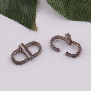 Op de afbeelding: Twee zilveren metalen gespen, een met een D-ringvorm en de andere met een lus.