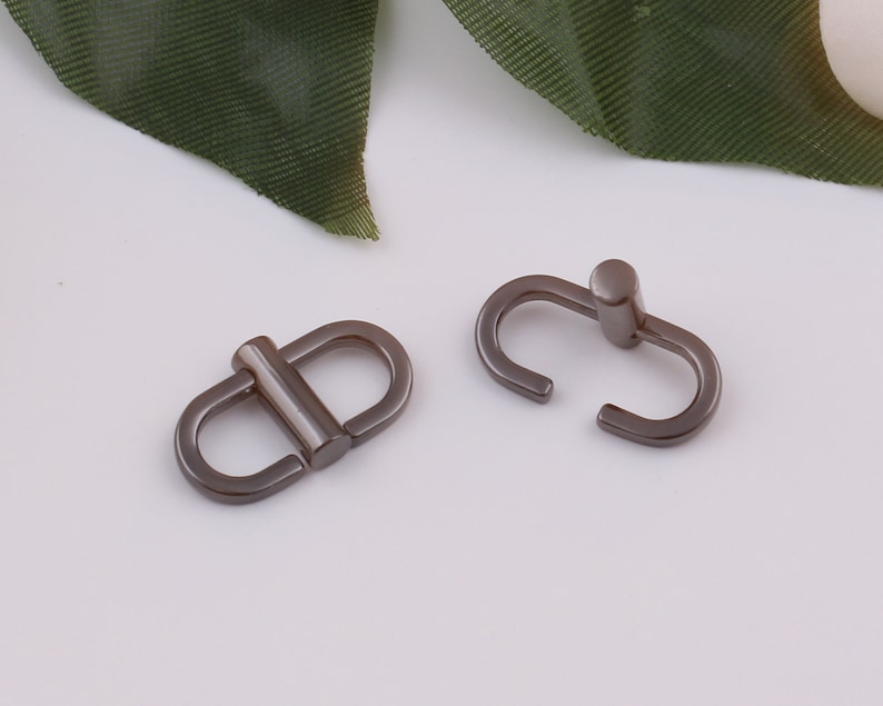 Op de afbeelding: Twee zilveren metalen gespen, een met een D-ringvorm en de andere met een lus.