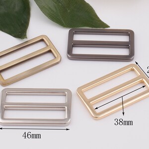 May include: Four metal slider buckles in different finishes: gold, silver, antique brass, and black. The buckles are rectangular with two parallel slots and measure 1.8 inches by 1.5 inches.