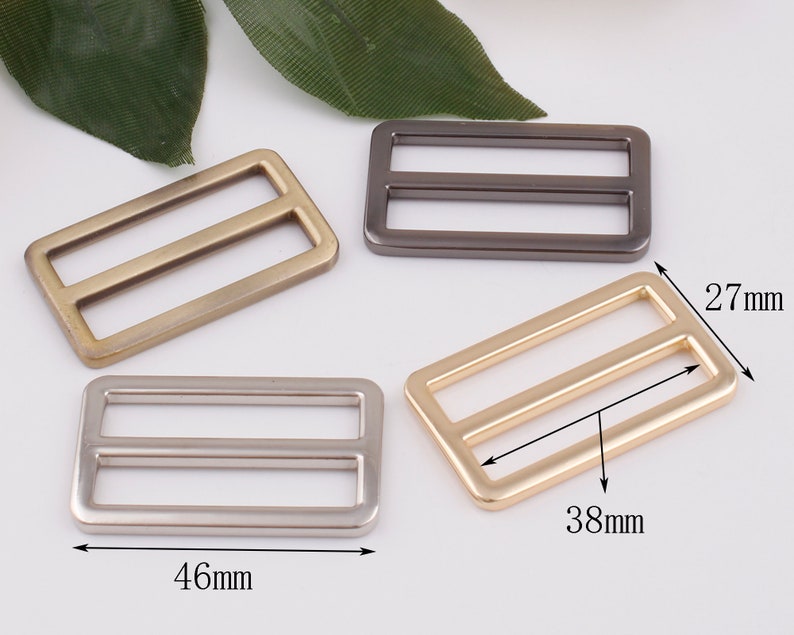 May include: Four metal slider buckles in different finishes: gold, silver, antique brass, and black. The buckles are rectangular with two parallel slots and measure 1.8 inches by 1.5 inches.