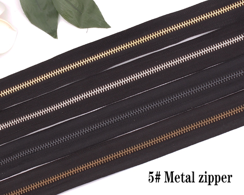 May include: Four black zipper tapes with different colored metal teeth. The teeth are gold, silver, black, and gold. The text "5# Metal zipper" is at the bottom of the image.