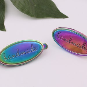 May include: Two iridescent oval metal tags with the word "handmade" embossed in a script font.