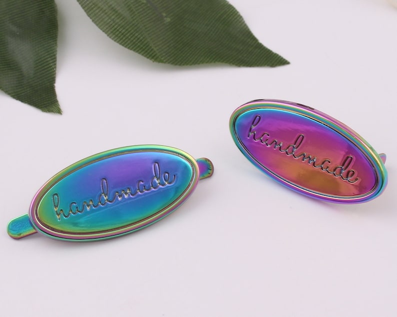 May include: Two iridescent oval metal tags with the word "handmade" embossed in a script font.