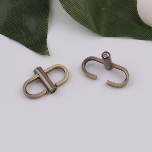 May include: Two antique gold-toned metal clasps with a swivel design. Each clasp has a small, clear rhinestone in the center.