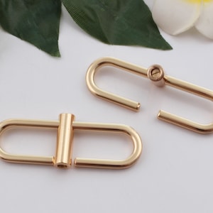 May include: Two gold-toned metal D-rings with a screw closure. The D-rings are oval-shaped and have a smooth finish.