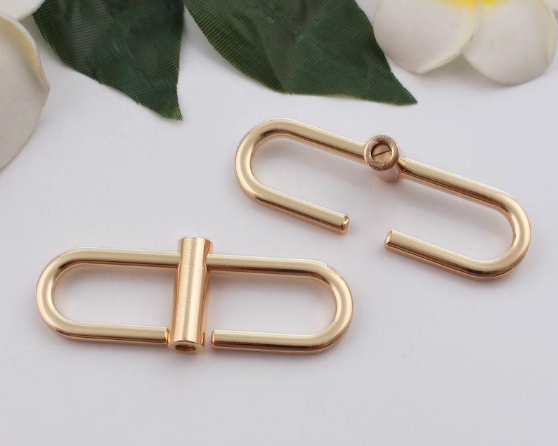 May include: Two gold-toned metal D-rings with a screw closure. The D-rings are oval-shaped and have a smooth finish.
