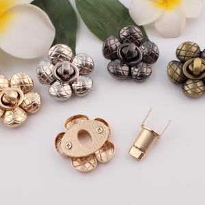 Könnte beinhalten: Fünf goldfarbene, blumenförmige Metallverschlüsse mit einem drehbaren Verschluss und ein goldfarbener Metallverschluss mit einem drehbaren Verschluss und einem separaten Stift.