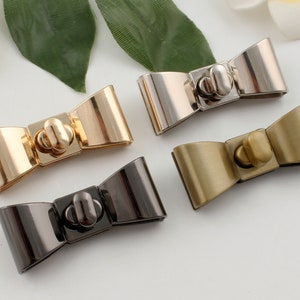 Op de afbeelding: Vier boogvormige metalen sluitingen in goud, zilver, zwart en messing afwerking. Elke sluiting heeft een kleine, ronde knop in het midden.