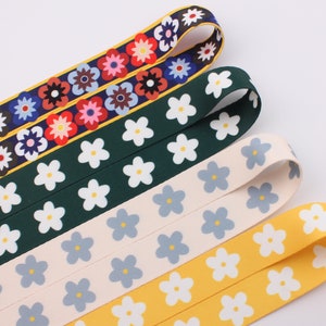Op de afbeelding: Vier verschillende gepatroneerde lintversieringen met witte bloemen op verschillende gekleurde achtergronden. De linten zijn groen, cr&egrave;me, geel en met een veelkleurig bloemenpatroon.