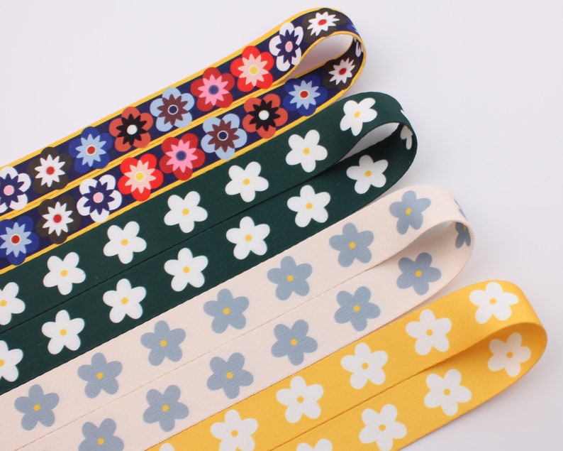Op de afbeelding: Vier verschillende gepatroneerde lintversieringen met witte bloemen op verschillende gekleurde achtergronden. De linten zijn groen, cr&egrave;me, geel en met een veelkleurig bloemenpatroon.