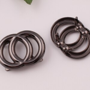 Pu&ograve; includere: Due anelli in metallo nero con un design a doppio anello. Gli anelli sono collegati da una piccola barra di metallo.