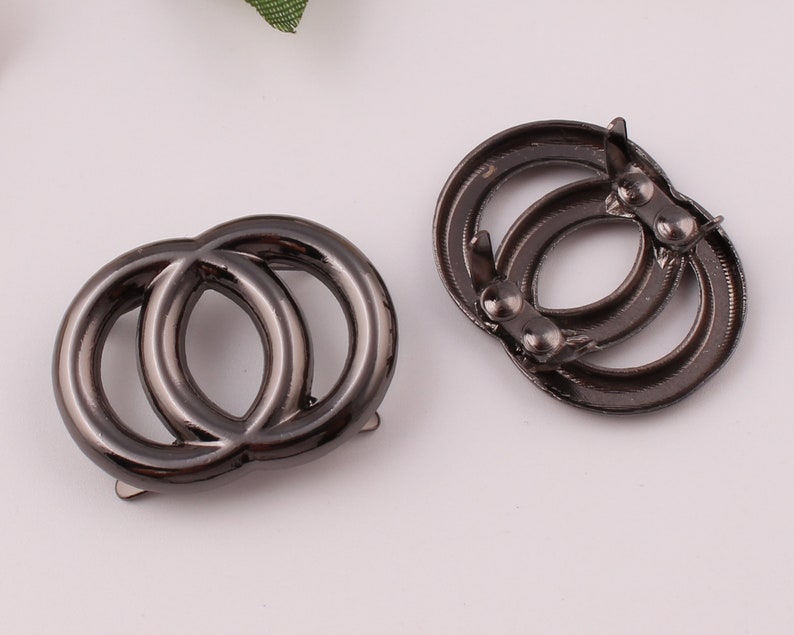Pu&ograve; includere: Due anelli in metallo nero con un design a doppio anello. Gli anelli sono collegati da una piccola barra di metallo.