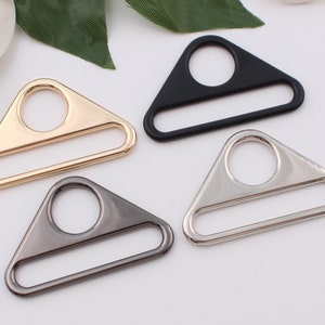 May include: Four triangle-shaped metal slider buckles in gold, silver, black, and gunmetal. Each buckle has a rectangular opening and a round hole.