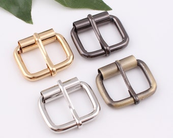 May include: Four metal belt buckles in different finishes: gold, silver, black, and antique brass. Each buckle has a square shape with rounded corners and a center bar.