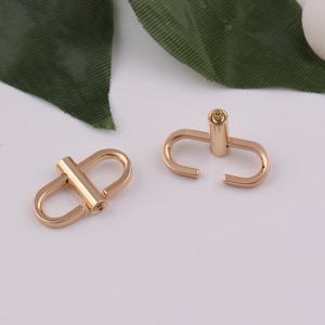 May include: Two gold-toned metal clasps with a small, round, gold-toned pin in the center of each clasp.