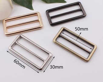 May include: Four metal belt buckle sliders in different finishes: gold, silver, black, and antique brass. The sliders are rectangular with two parallel bars across the center. The measurements are 60mm x 30mm and 50mm x 30mm.