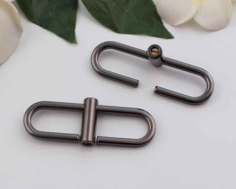 May include: Two gunmetal gray metal D-rings with a screw closure. The D-rings are about 1 inch in diameter.