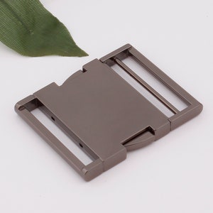 May include: A gunmetal gray metal buckle with a sliding closure. The buckle has two slots for a strap.