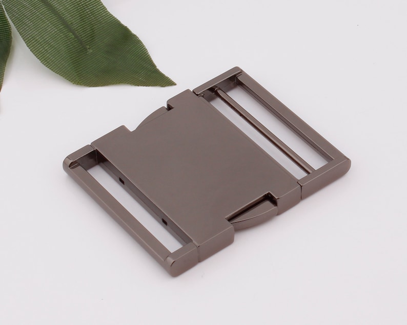 May include: A gunmetal gray metal buckle with a sliding closure. The buckle has two slots for a strap.