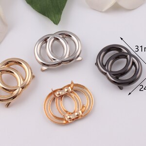 Pu&ograve; includere: Tre chiusure metalliche a doppio anello in oro, argento e nero. Le chiusure misurano circa 31 mm di larghezza e 24 mm di altezza.