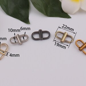 Op de afbeelding: Vier metalen gespen in verschillende maten en afwerkingen. De gespen zijn zilver, goud en zwart. De gespen zijn 10 mm, 6 mm, 13 mm, 4 mm, 22 mm en 19 mm groot.