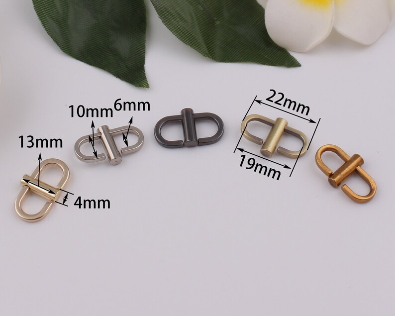 Op de afbeelding: Vier metalen gespen in verschillende maten en afwerkingen. De gespen zijn zilver, goud en zwart. De gespen zijn 10 mm, 6 mm, 13 mm, 4 mm, 22 mm en 19 mm groot.